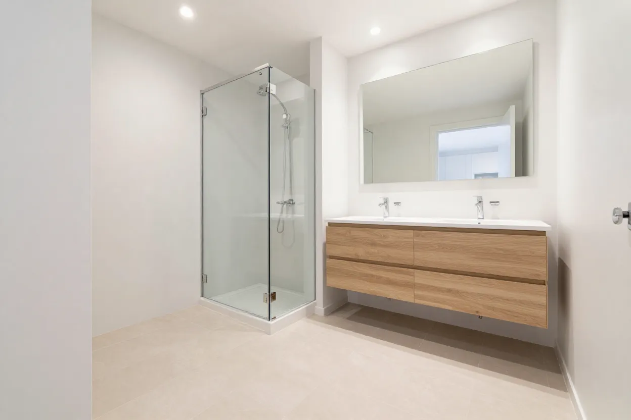 Banheiro compacto com revestimento claro contínuo, box de vidro transparente e espelho amplo